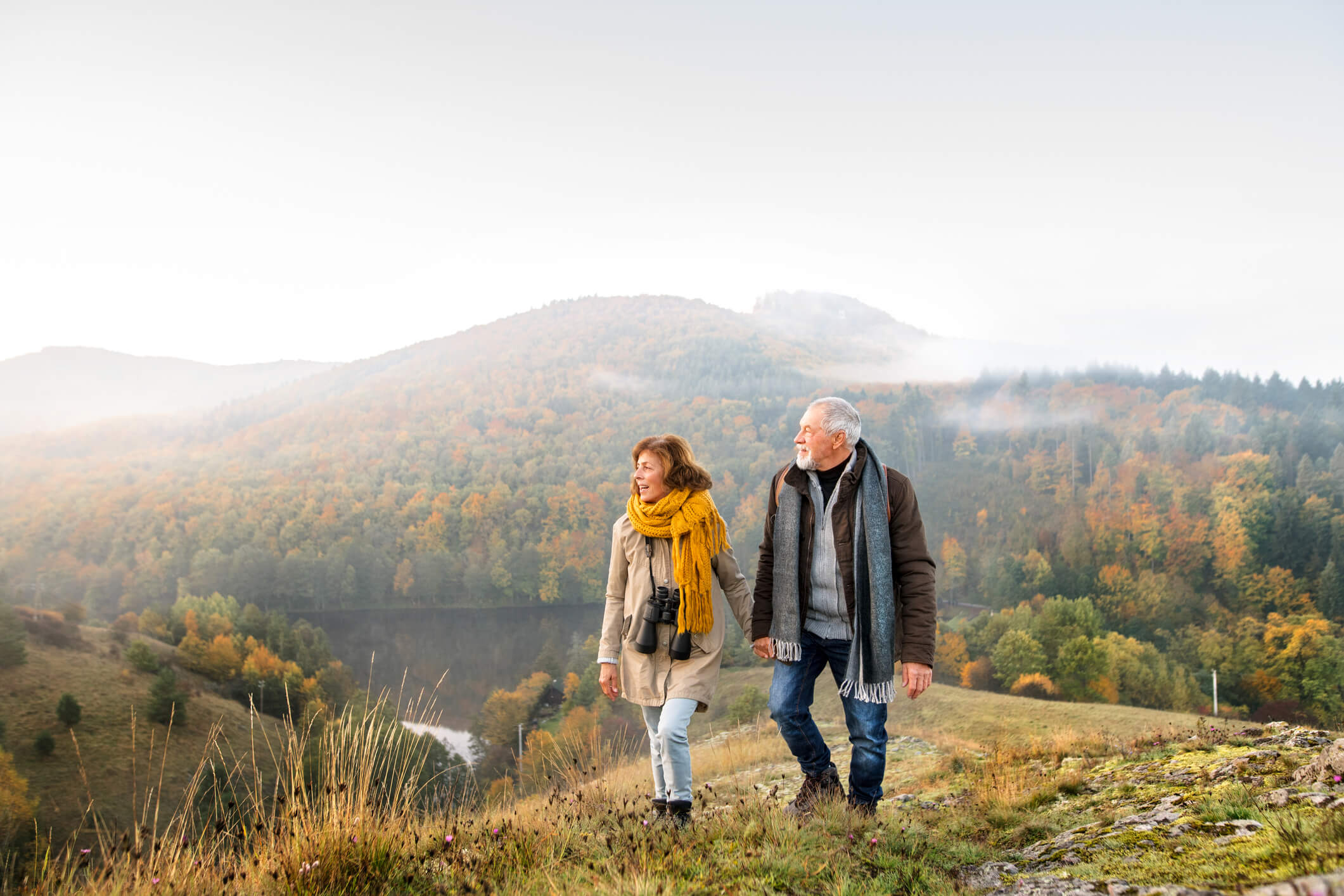 a retired couple hiking up a hill next to a lake and overlooking the hill on a cloudy day